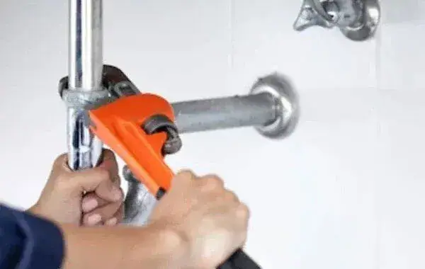 Hände ziehen mit einer Rohrzange die Verschraubung einer Wasserleitung nach