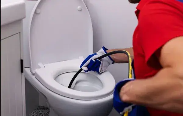 Installateur mit Schutzhandschuhen führt eine Reinigungsspirale in eine Toilette ein